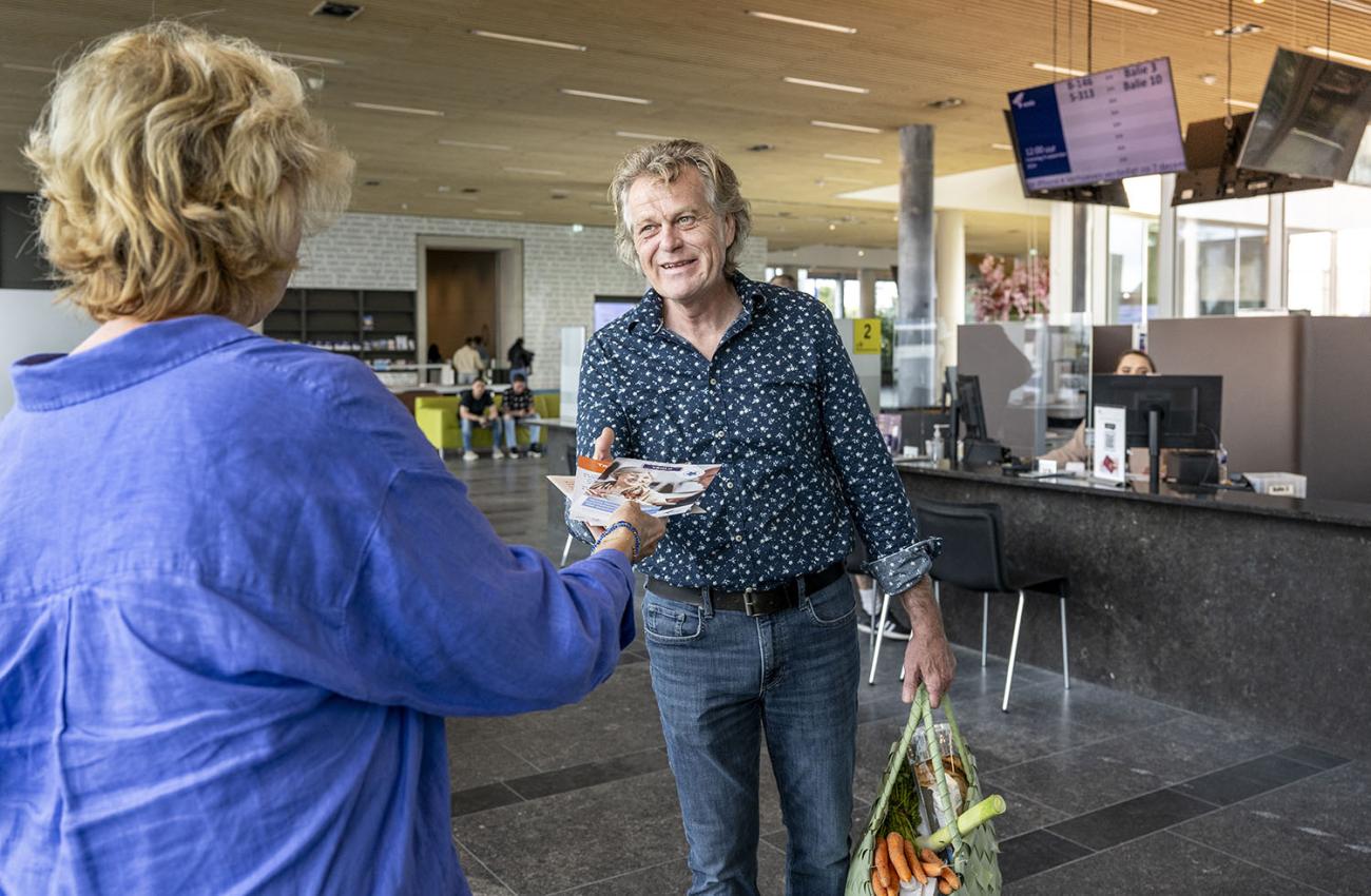 Man met boodschappentas bij stadkantoor gemeente Venlo krijgt folders aangereikt door een vrouwelijke medewerker
