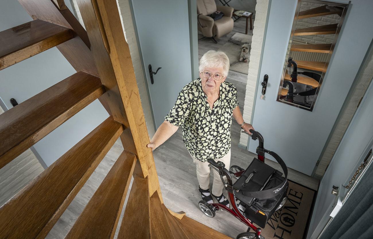 Vrouw met rollator voor trap in hal van woning