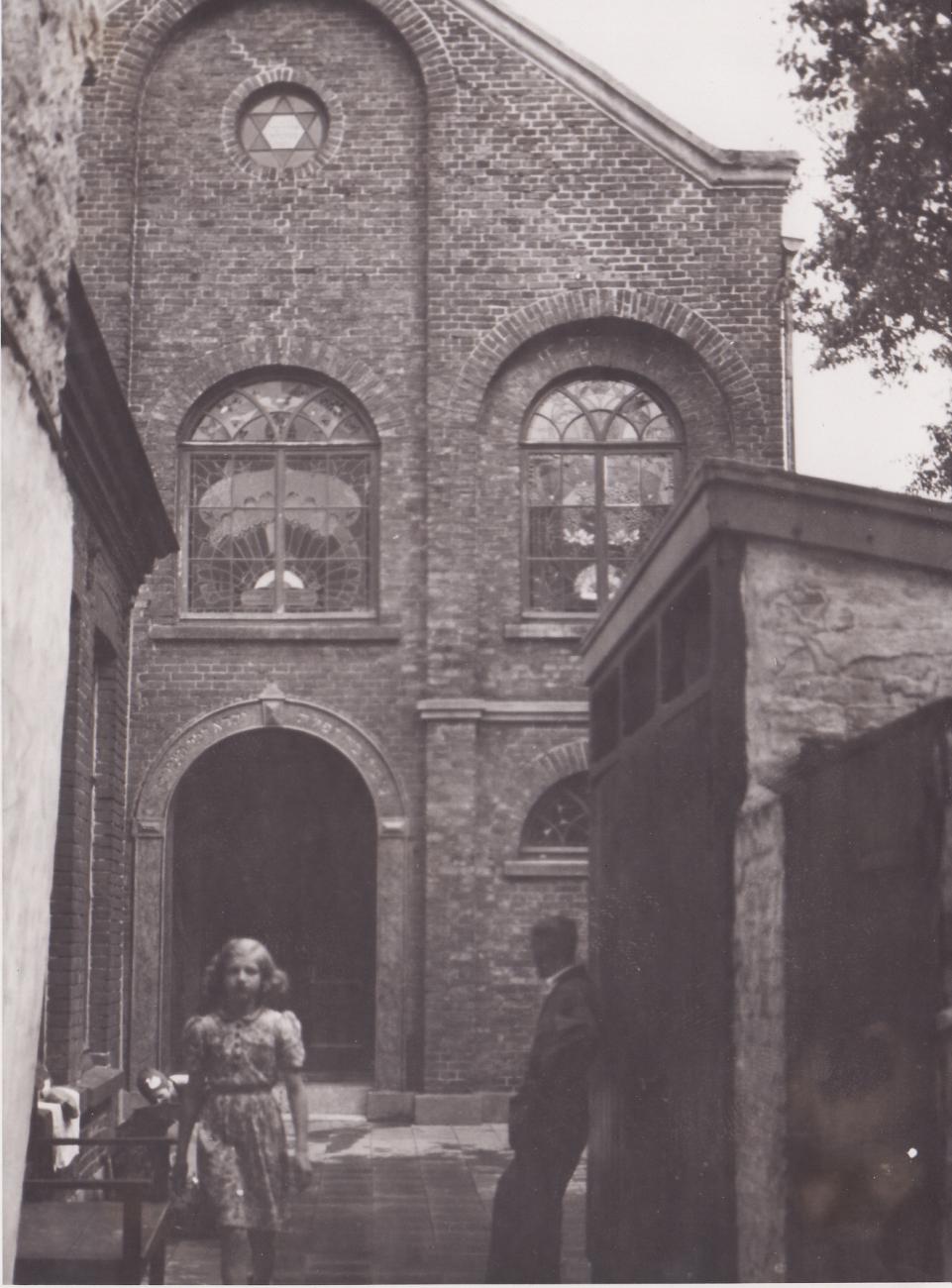De voorgevel van een Joodse synagoge met een jong meisje ervoor, ten tijde van de Tweede Wereldoorlog