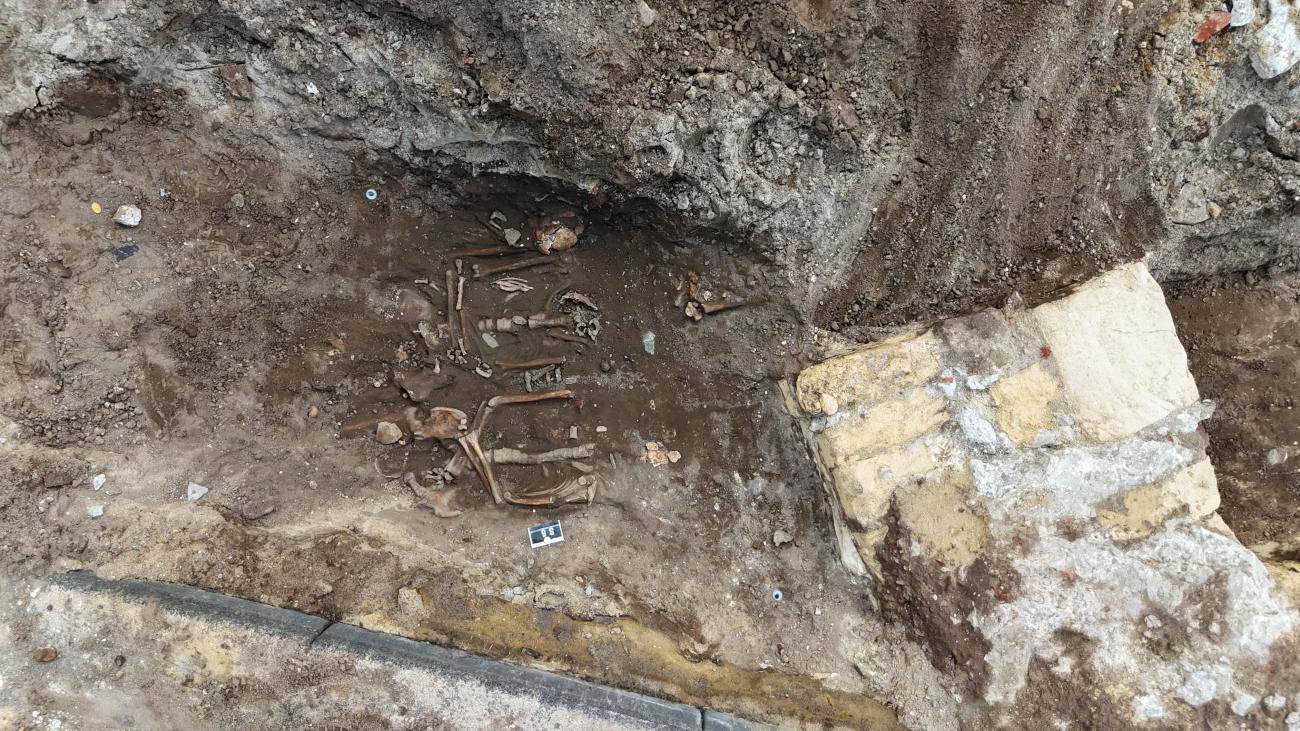 Een steunbeer van mergel de middeleeuwse Lambertuskerk (rechts) met links daarvan een aantal menselijke skeletten.