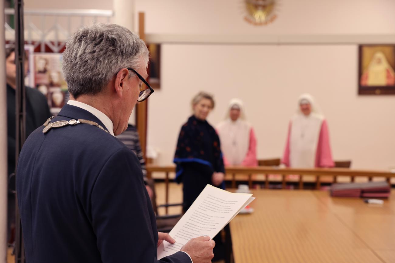 Burgemeester speecht met roze zusters op de achtergrond