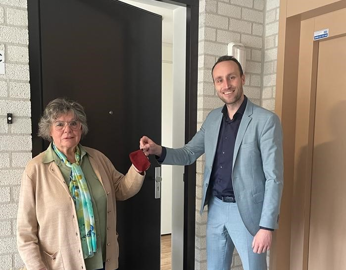 Wethouder Tom Verhaegt overhandigt de sleutel van de nieuwe woning van mevrouw Bovendeerd voor haar voordeur.