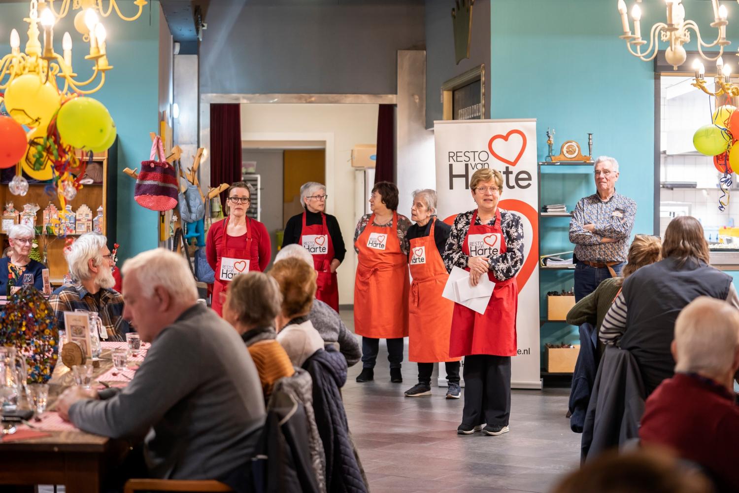 Vrijwilligers van Resto VanHarte spreken gasten toe tijdens een gezellige maaltijd.