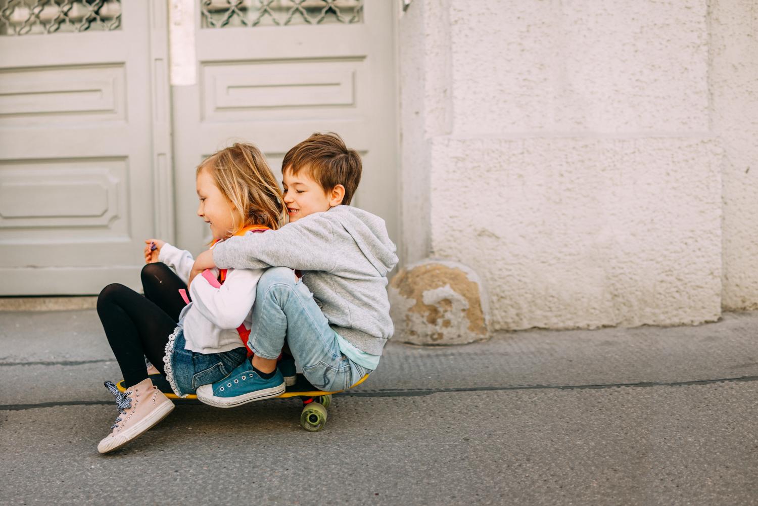 Foto van een jongentje en meisje die samen knuffelend op een skateboard zitten