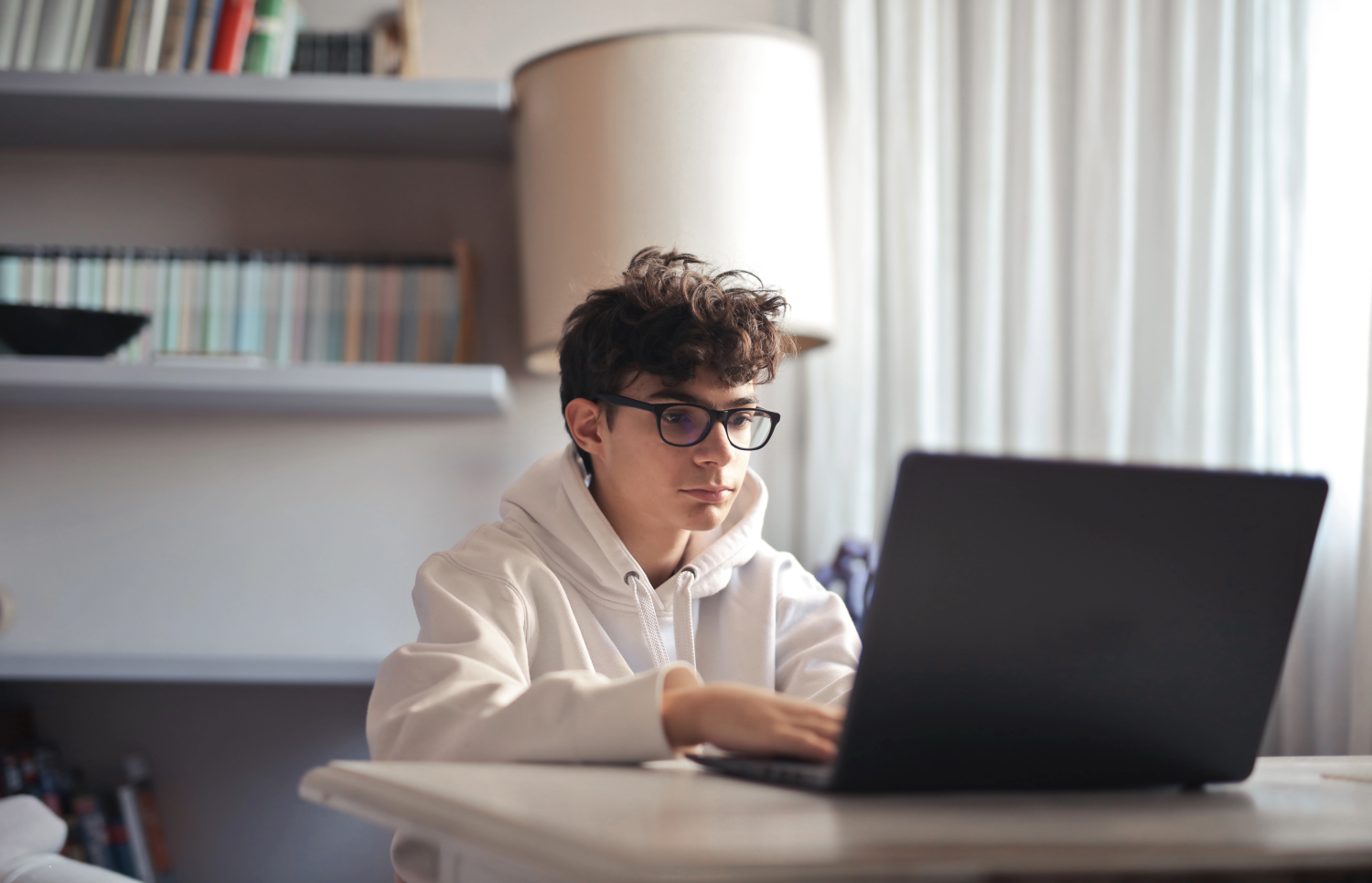 jongen met bril en witte hoodie kijkt naar laptop