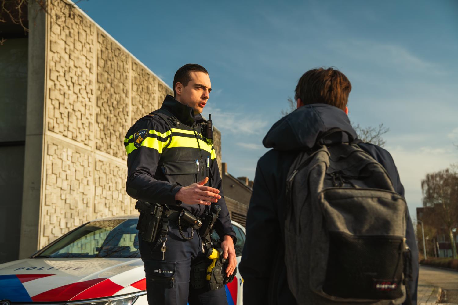 Een agent die een jongere met rugzak toespreekt