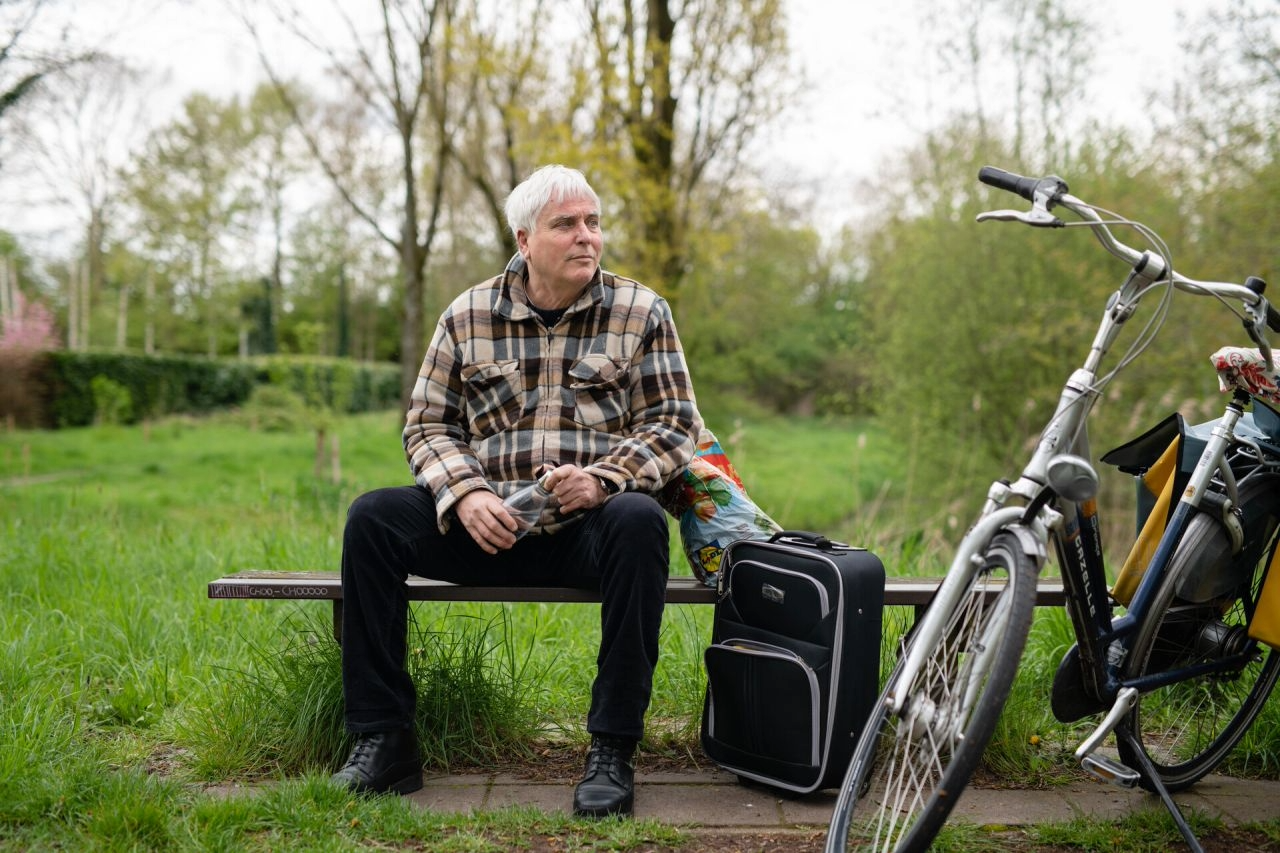 een dakloze man op een bankje met zijn fiets en een koffer