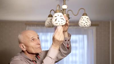 Een meneer die in een woonkamer een lamp vervangt.