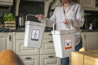 Een mevrouw in een keuken die twee afvalbakken vasthoudt voor het scheiden van afval.