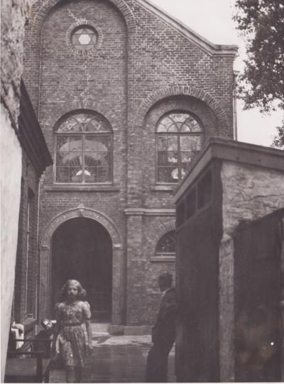 De voorgevel van een Joodse synagoge met een jong meisje ervoor, ten tijde van de Tweede Wereldoorlog