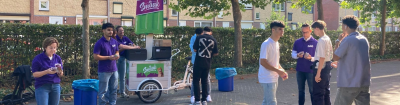 De ijscokar van de campagne Betaal later kater, omringd door enkele leerlingen en wethouder Erwin Boom die helpt om de ijsjes uit te delen.