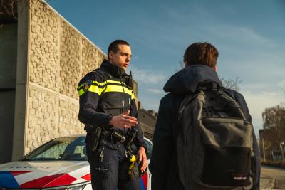 Een agent die een jongere met rugzak toespreekt