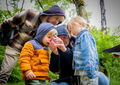 twee volwassenen en twee kinderen die samen een plastic doosje bekijken waar een beestje uit het bos in kan